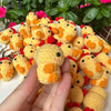 A hand holds a cluster of handmade crochet yellow and orange duck or chick animals.