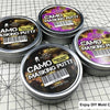 Four tins of Camo Masking Putty for model painting displayed on a grid background.