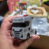 A hand holds a silver 1:64 scale RC drift truck model with a black cab and grille.