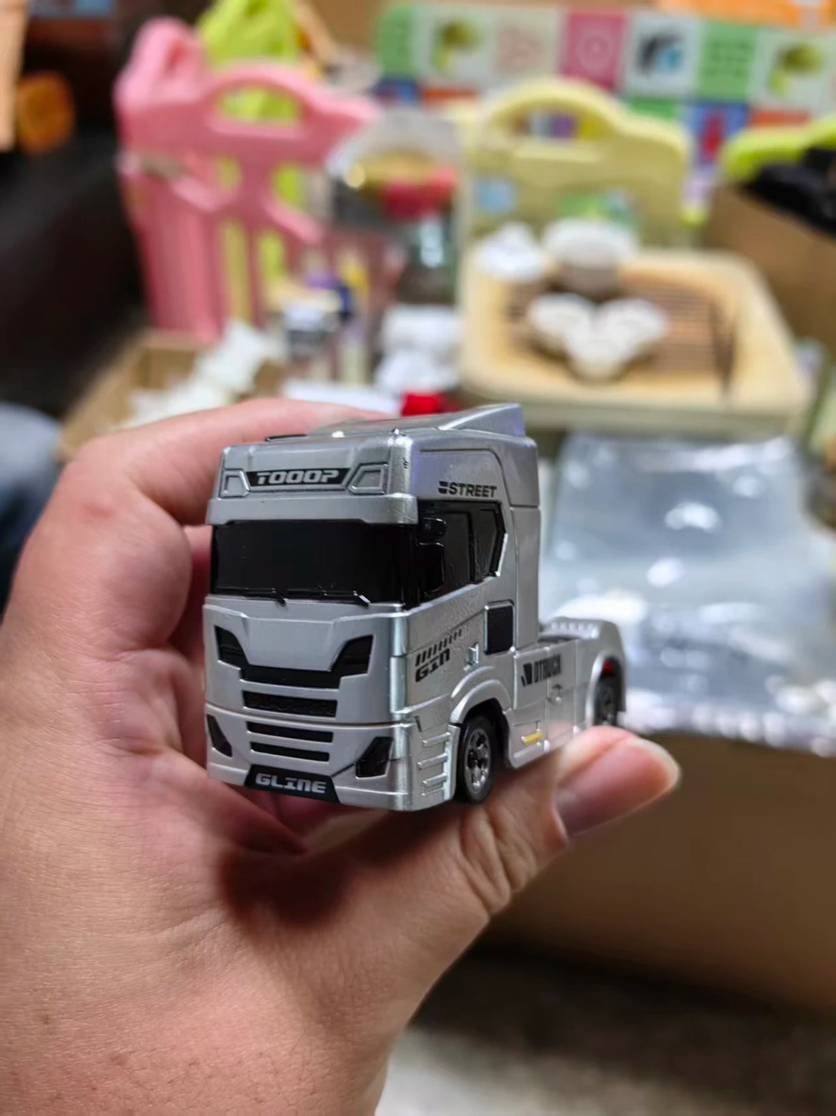A hand holds a silver 1:64 scale RC drift truck model with a black cab and grille.