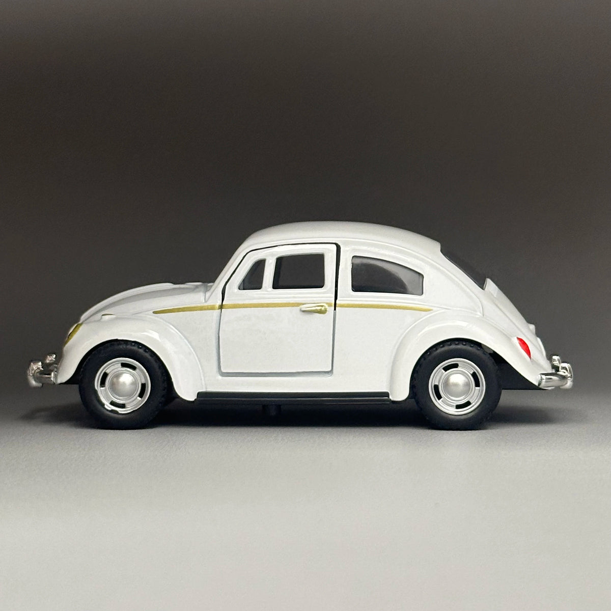 A white diecast model of a classic retro Beetle with gold accents, shown in profile view.