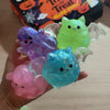 A collection of colorful ghost and bat squeeze stress relief balls in purple, green, and pink are held in a hand.