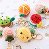 A collection of colorful handmade crochet fruit keychain pendants including watermelon, strawberry, and kiwi.