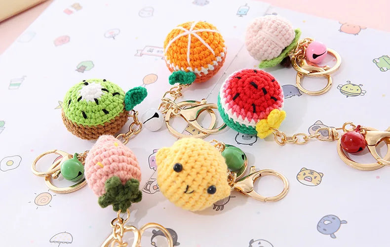 A collection of colorful handmade crochet fruit keychain pendants including watermelon, strawberry, and kiwi.