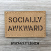 Un patch rectangulaire beige tissé avec le texte SOCIALLY AWKWARD imprimé en noir.