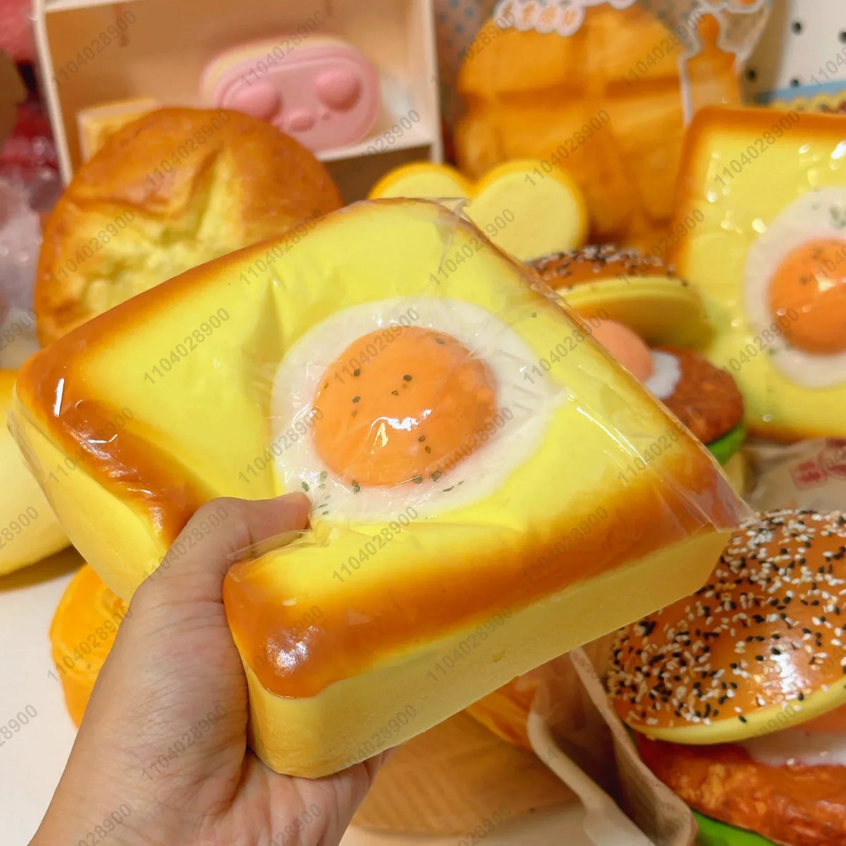 A hand holds a yellow squishy fried egg toast stress relief toy next to other food items.