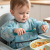 A baby is using a full-sleeve waterproof bib with a cute cartoon design to feed food.