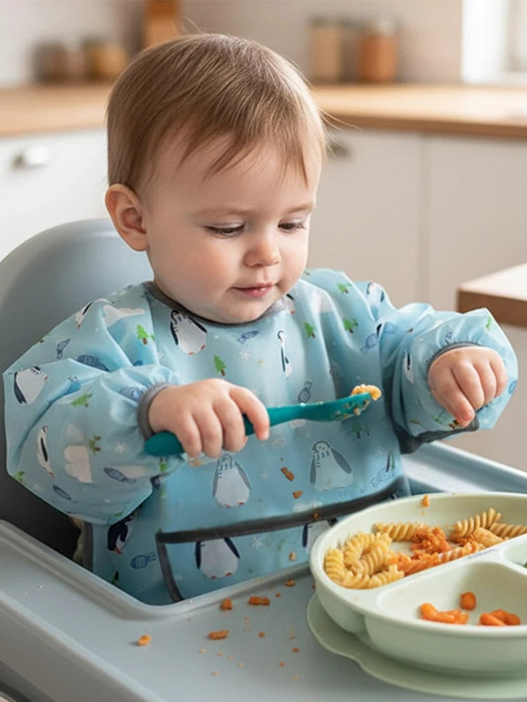 A baby is using a full-sleeve waterproof bib with a cute cartoon design to feed food.
