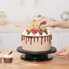 A round cake decorated with chocolate ganache and fresh berries, being prepared by a hand.