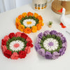 Three hand-crocheted lily of the valley coasters in orange, red, and purple on a white table.