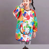 A young girl wearing a colorful, hand-painted art smock over her clothes.