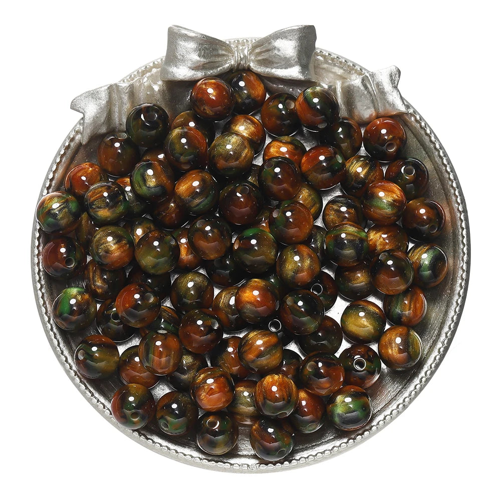A pile of round, iridescent brown and green glitter resin beads in a silver dish for jewelry making