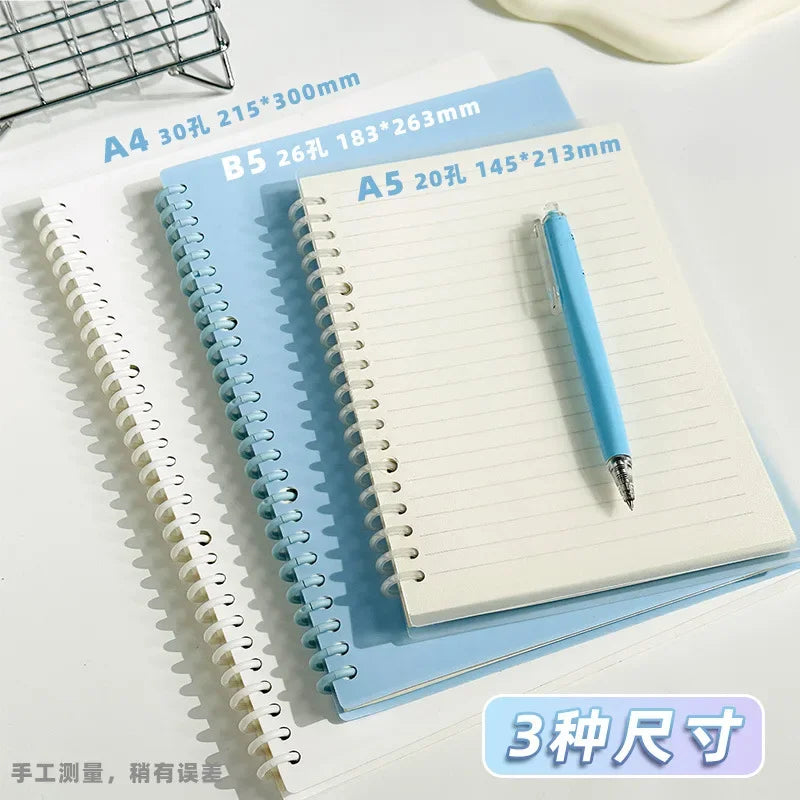 A set of three spiral notebooks in different sizes A4 B5 and A5 lying on a white surface.