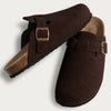 A pair of dark brown suede cork mules with leather straps and arch support.