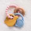A set of food-grade silicone planet teethers for babies in pink, wood, and blue colors resting on white granular material.