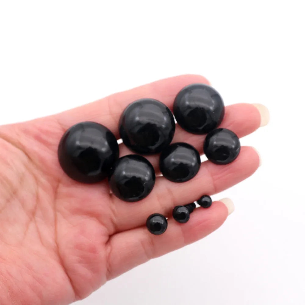 A hand holds several black plastic safety eyes with washers for crafting.