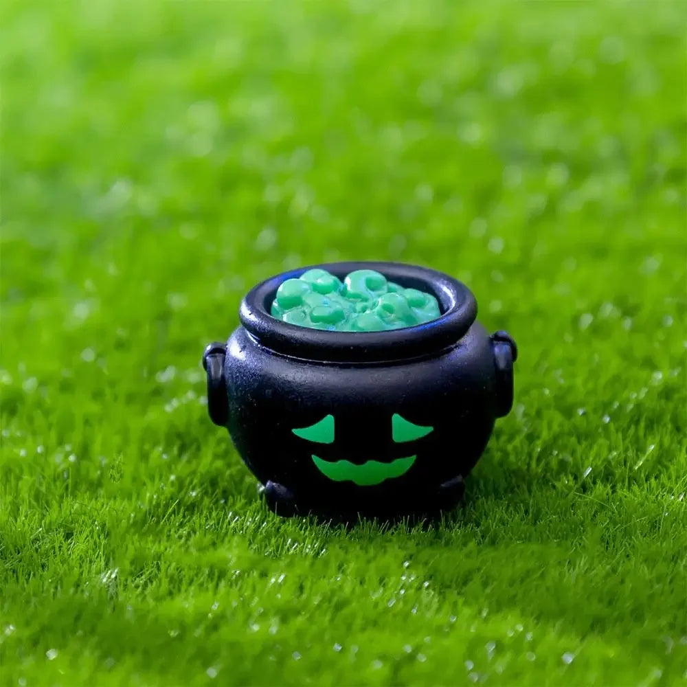 A black pumpkin bear figurine with a green smiling face and a bowl of green candies sitting on bright green grass.