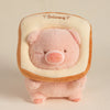 A pink plush pig stuffed animal with a light beige hood and embroidered text