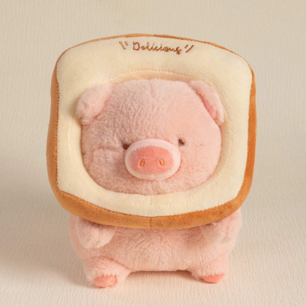 A pink plush pig stuffed animal with a light beige hood and embroidered text