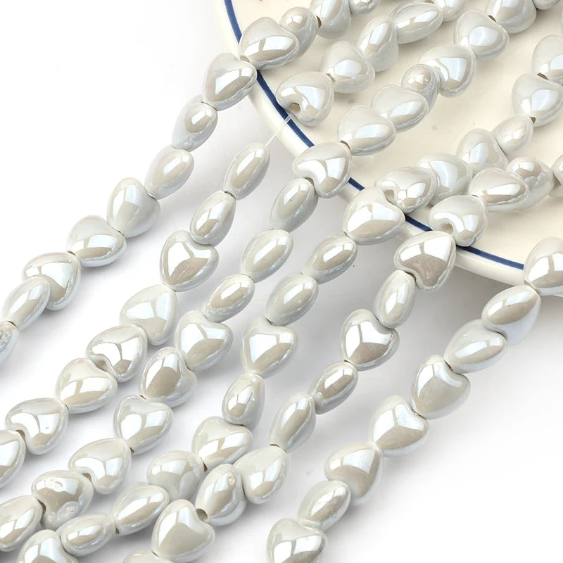 A collection of small, heart-shaped acrylic beads in white and gray are displayed on a light blue surface.