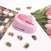 A pink lever action embosser tool rests on a white surface surrounded by pressed floral and leaf elements.