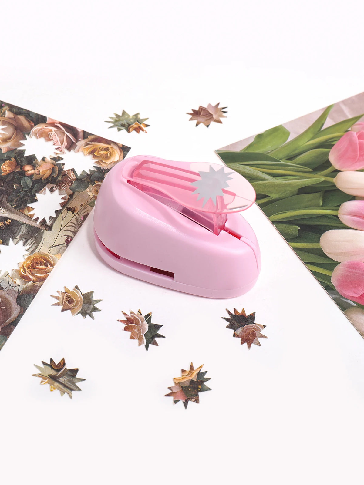 A pink lever action embosser tool rests on a white surface surrounded by pressed floral and leaf elements.