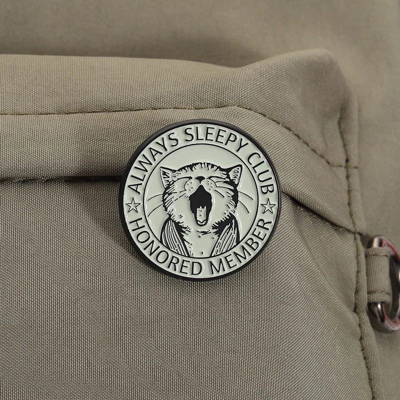 An enamel pin featuring a stylized, yawning cat design with the text Always Sleepy Club Honored Member