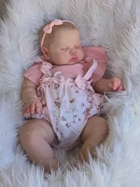 A newborn baby doll with hand-painted skin is lying in white fluffy fur.