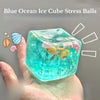 Une main tient une balle anti-stress bleue translucide remplie de paillettes et de créatures marines.