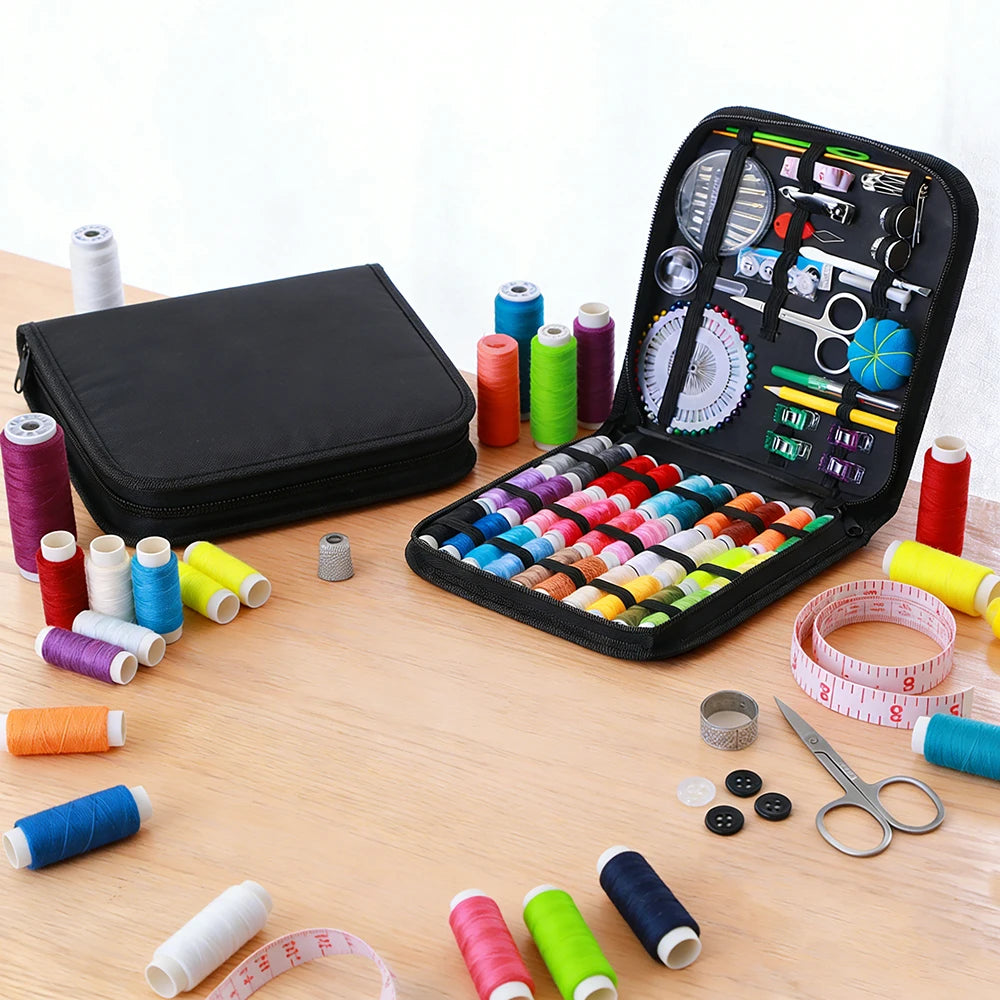 A complete sewing kit with various threads, needles, and tools is displayed in an open black storage box on a wooden surface.