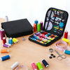 A complete sewing kit with various threads, needles, and tools is displayed in an open black storage box on a wooden surface.