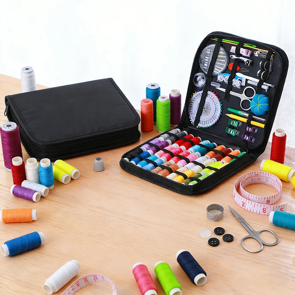 A complete sewing kit with various threads, needles, and tools is displayed in an open black storage box on a wooden surface.