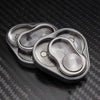 A silver metal fidget slider with three nested, oval-shaped magnetic components resting on a dark carbon fiber surface.