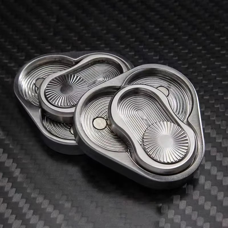 A silver metal fidget slider with three nested, oval-shaped magnetic components resting on a dark carbon fiber surface.
