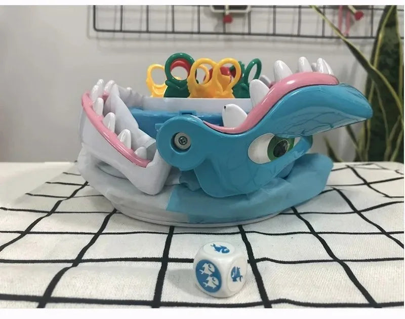 A colorful shark bite prank board game with plastic teeth and a blue body is displayed on a white checkered cloth.