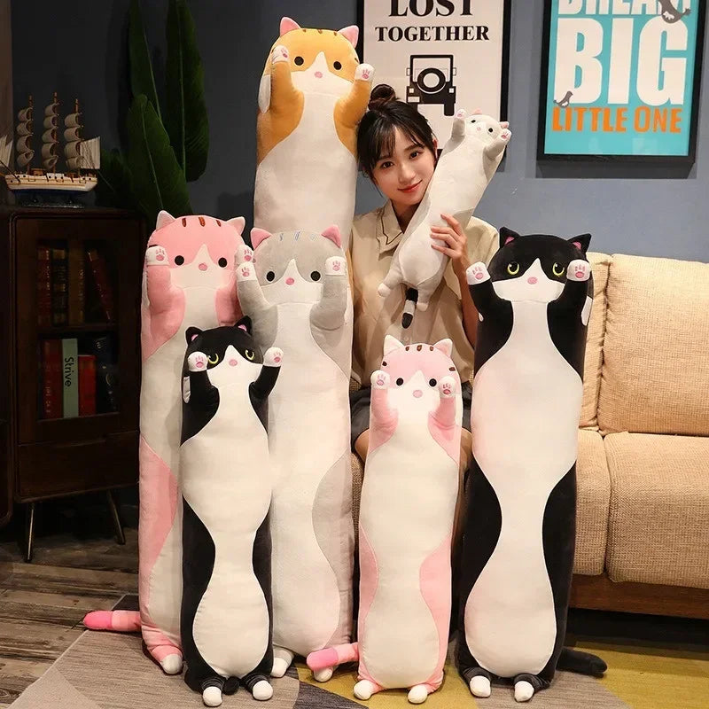 A collection of plush cat pillows in various colors including orange, pink, and black sitting on a sofa.