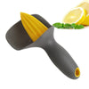 A dark gray manual citrus juicer with a yellow citrus wedge and a slice of lemon in the background.