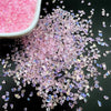 Pink crushed glass crystals scattered on a black surface.