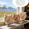 A set of white ceramic candle molds shaped like horses with Celtic knot designs displayed on a shelf by a window.