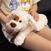 Una persona sostiene un peluche de perro de osito blanco con detalles marrones, vistiendo una blusa de color claro.