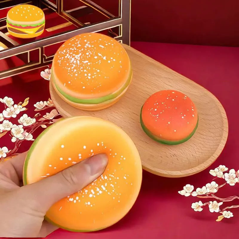 A hand holds an orange squishy hamburger stress ball with white sprinkles on a wooden surface.