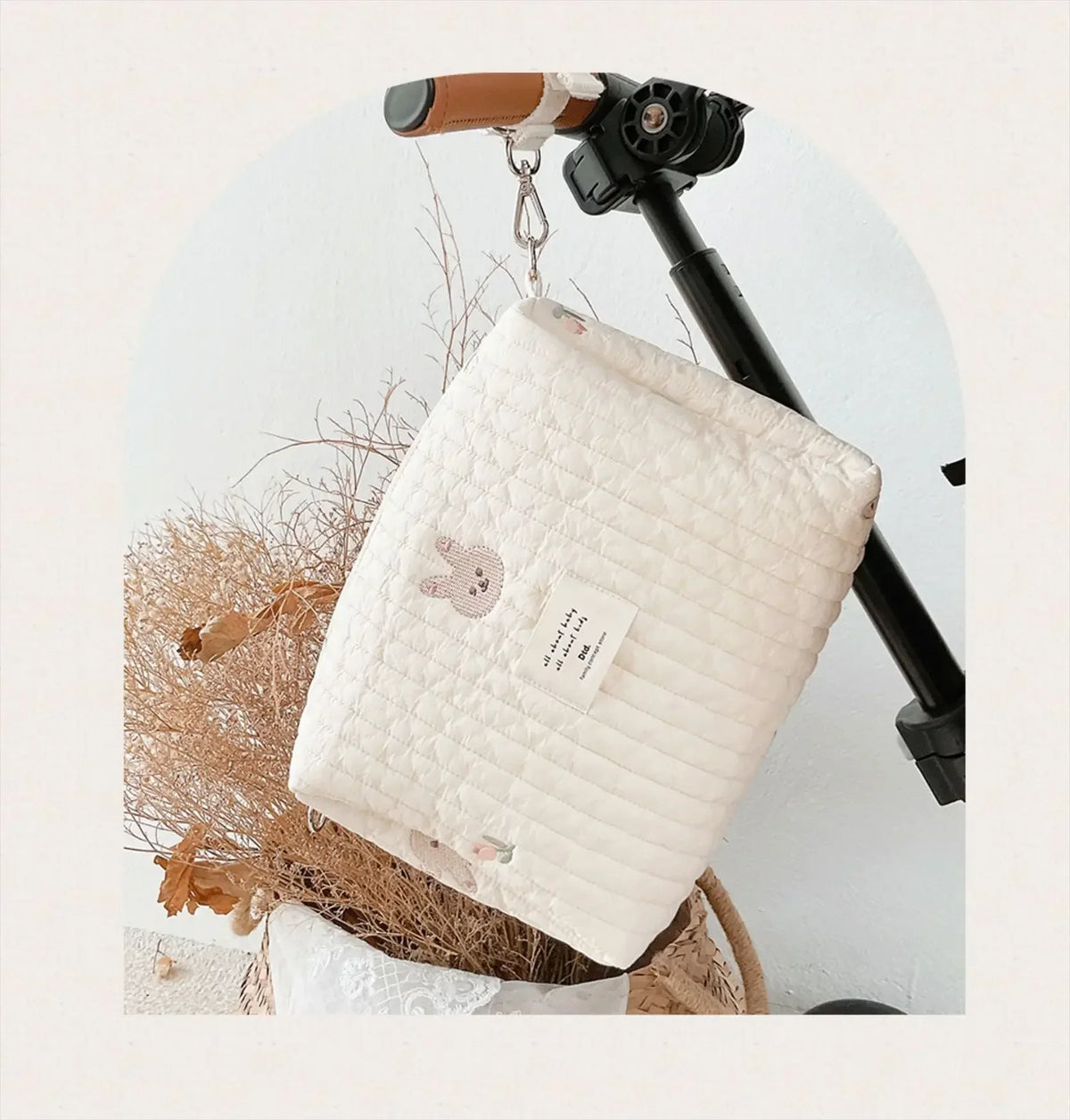 A quilted white baby diaper caddy organizer hanging from a black stroller strap mount.