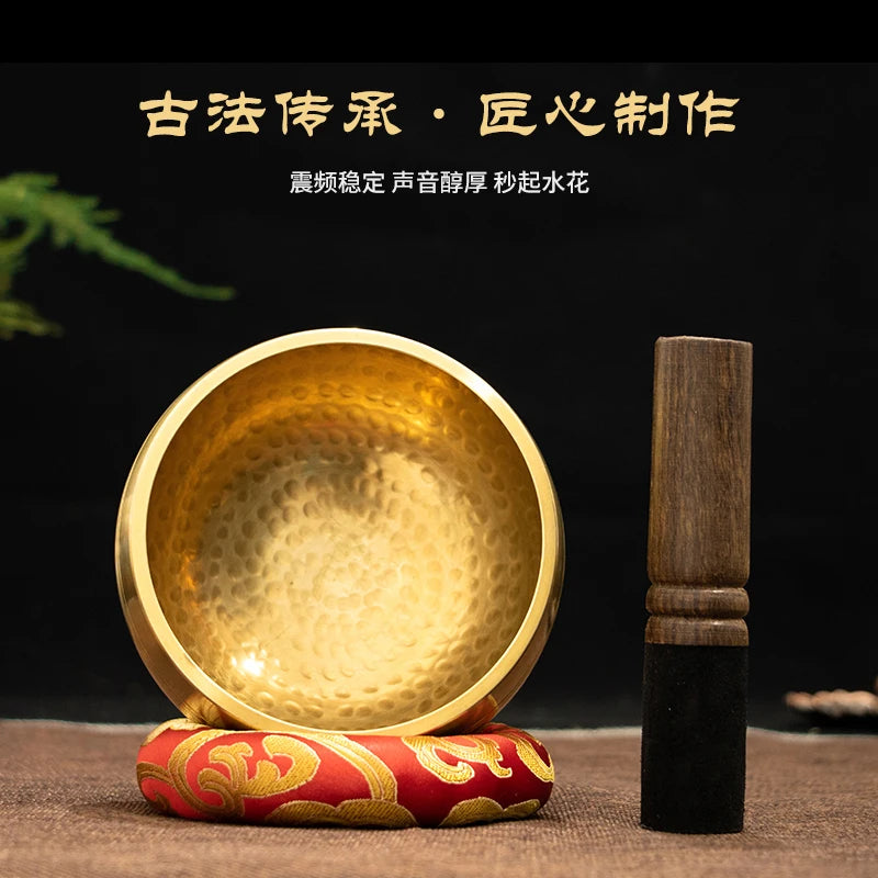 Handmade copper singing bowl with a wooden mallet resting on a red fabric.
