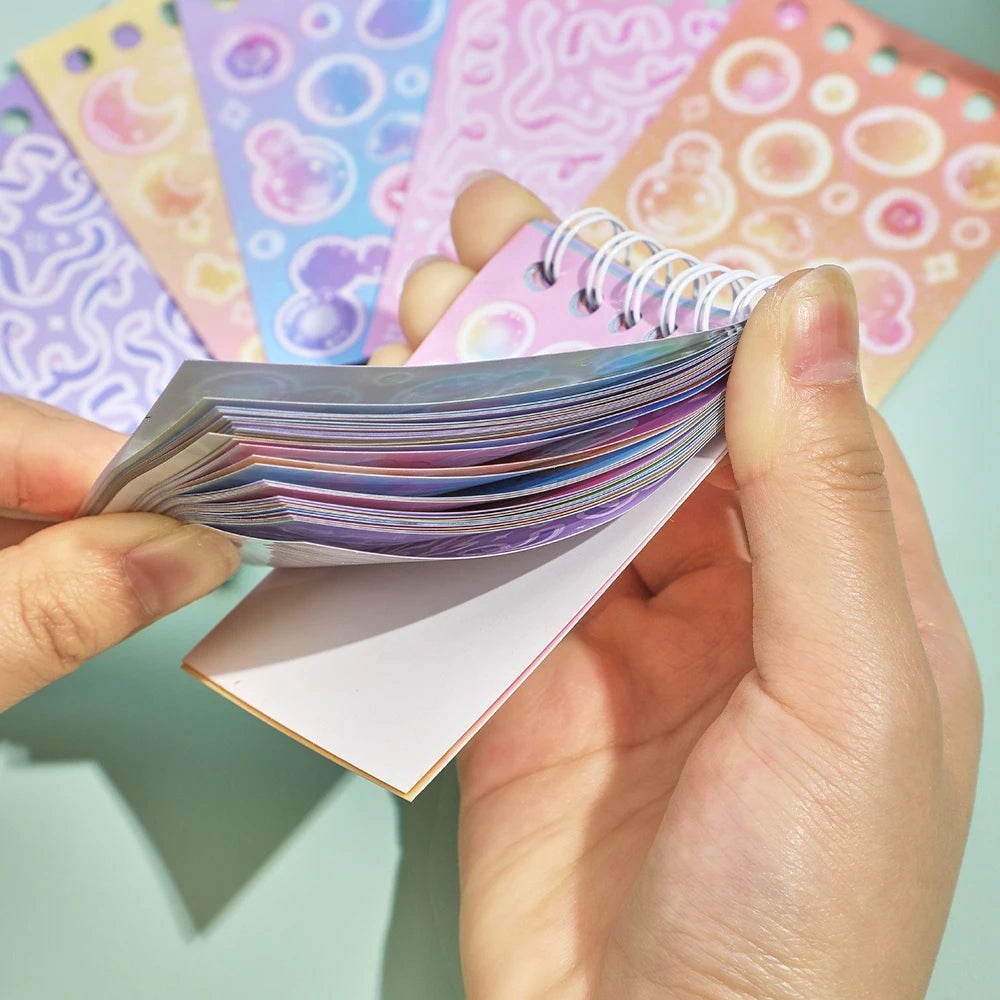 A hand holds a stack of colorful fantasy aesthetic stickers and a pink card featuring more designs.