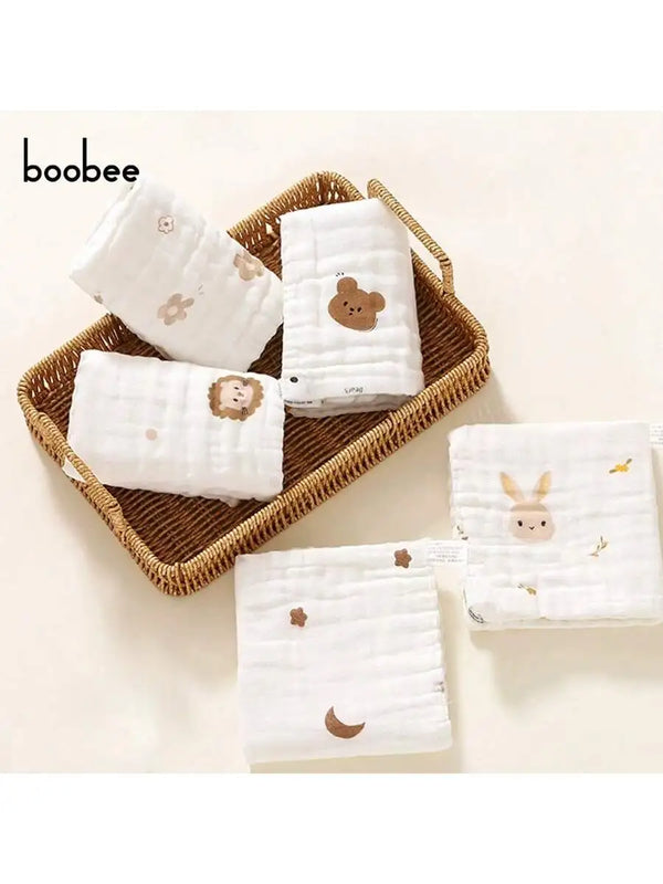 Set aus fünf weißen, ultraweichen Babytüchern mit niedlichen Tierdesigns, präsentiert in einem geflochtenen Korb.