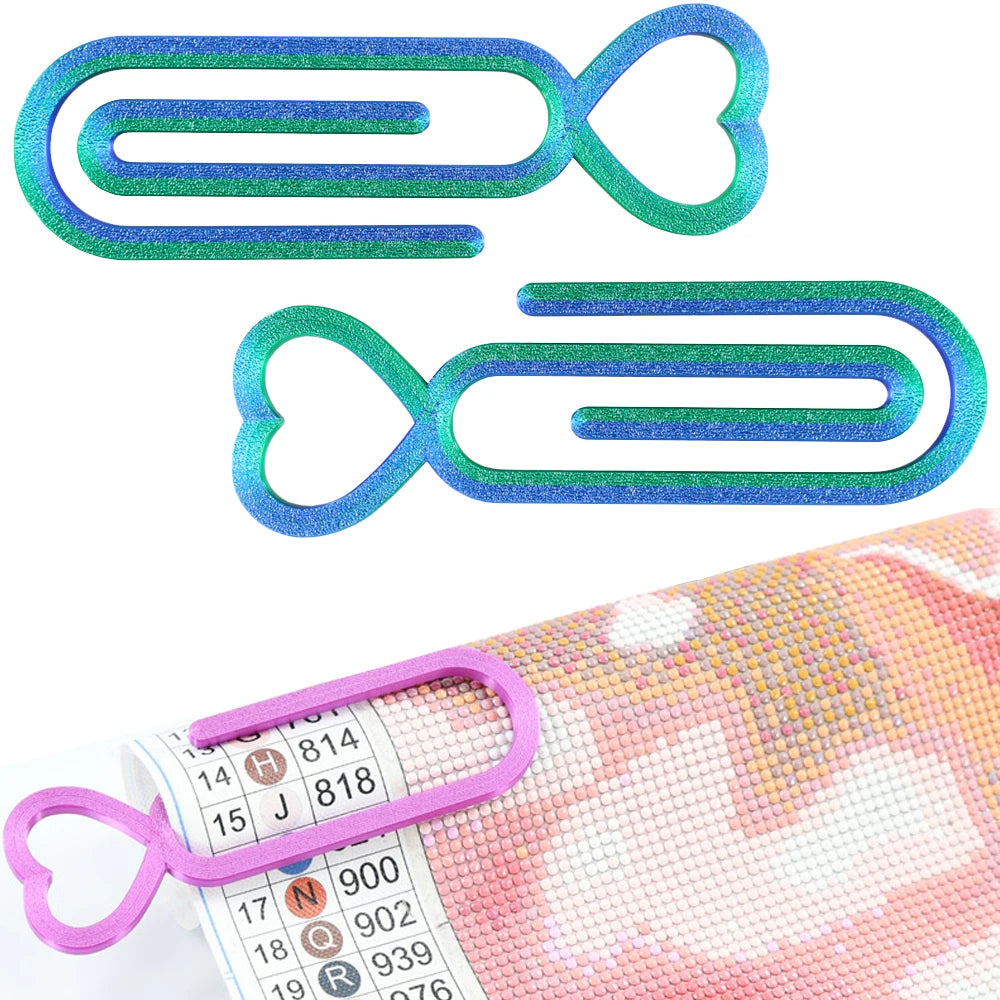 Two heart-shaped clear plastic clips used for diamond painting canvas