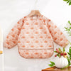 A light pink long-sleeved baby bib with a rainbow pattern hanging on a wooden hanger.