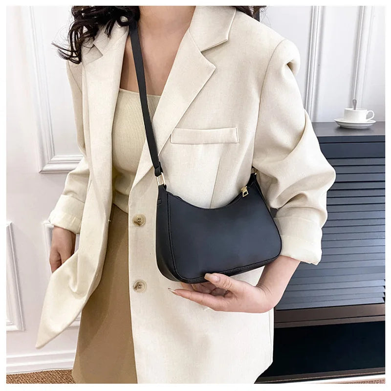A woman wearing a beige blazer and tan dress holds a black PU square crossbody bag.
