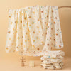 A set of two white baby gauze swaddle blankets with small animal patterns hanging on a wooden rod.