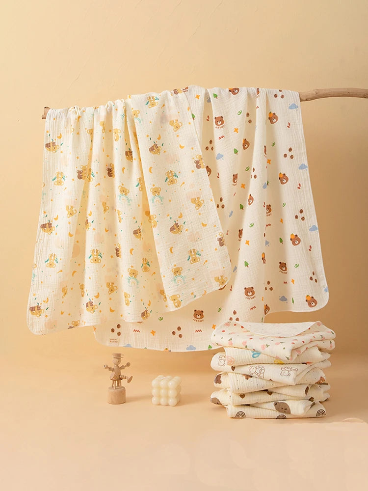 A set of two white baby gauze swaddle blankets with small animal patterns hanging on a wooden rod.